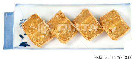 Four pieces of traditional Asian mung bean cake with melon seeds served on a decorative white and blue ceramic plate Isolated. Professional top view for food packaging. Four pieces of traditional Asian mung bean cake with melon seeds served on a decorative white and blue ceramic plate Isolated. Professional top view for food packaging. 142573032
