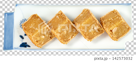 Four pieces of traditional Asian mung bean cake with melon seeds served on a decorative white and blue ceramic plate Isolated. Professional top view for food packaging. Four pieces of traditional Asian mung bean cake with melon seeds served on a decorative white and blue ceramic plate Isolated. Professional top view for food packaging. 142573032
