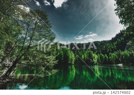 Dark moody mountain lake, dense green forest. Mystery landscape with river and fir woods, sulking and silence scenery 142574802