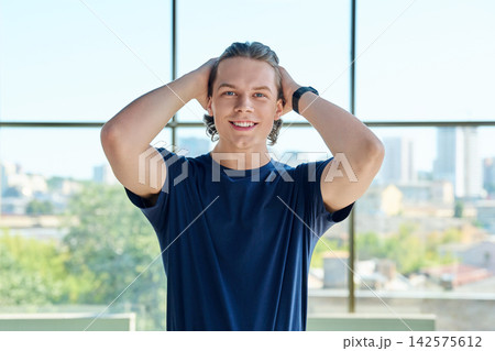 Young male student holding hands behind head smiling looking at camera near window 142575612