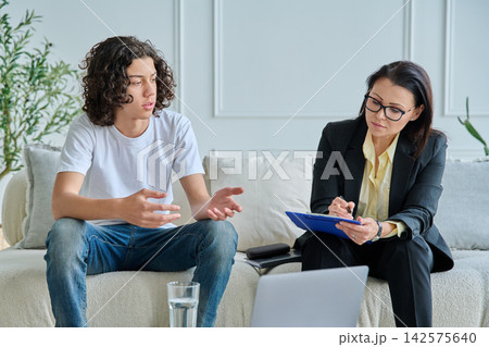 Psychologist listening to teenage boy in office 142575640