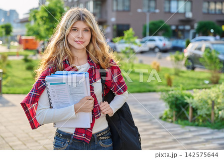 Young blonde female student holding textbooks and backpack outdoors in the city Young blonde female student holding textbooks and backpack outdoors in the city 142575644