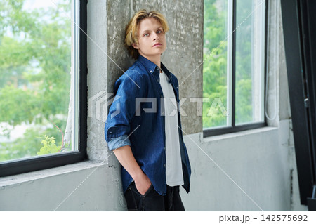Handsome teenage boy looking at camera, near modern window Handsome teenage boy looking at camera, near modern window 142575692