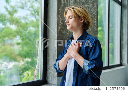 Peaceful young man with hands on chest closed eyes Peaceful young man with hands on chest closed eyes 142575696