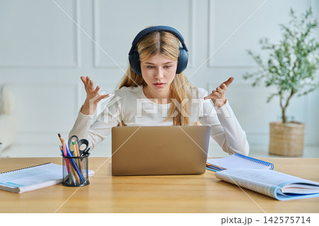 Focused teenage girl in headphones studying with laptop Focused teenage girl in headphones studying with laptop 142575714
