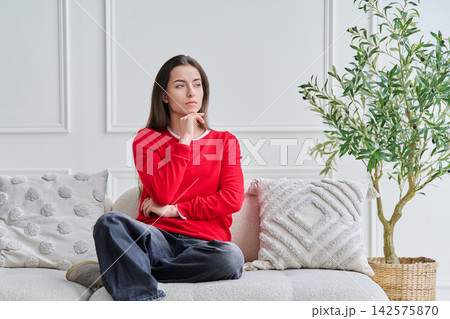 Portrait of beautiful, dreaming, pensive young teenage girl sitting on sofa Portrait of beautiful, dreaming, pensive young teenage girl sitting on sofa 142575870