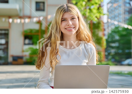 Smiling teenage girl with laptop on school campus 142575930