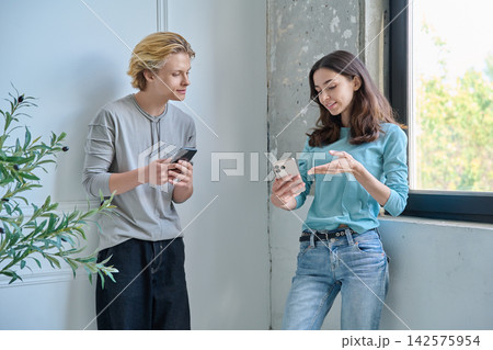 Teen friends talking to each other holding cellphones Teen friends talking to each other holding cellphones 142575954
