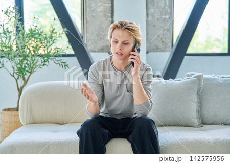 Young blonde man sitting on a comfortable sofa and talking on mobile phone 142575956