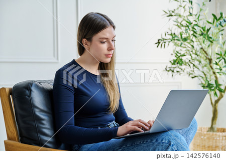 Portrait of young woman sitting on chair with laptop Portrait of young woman sitting on chair with laptop 142576140