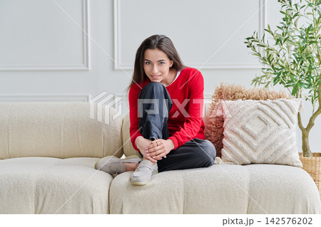 Portrait of beautiful young teenage girl sitting on sofa looking at camera Portrait of beautiful young teenage girl sitting on sofa looking at camera 142576202