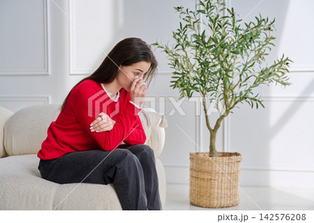 Sad unhappy crying young woman sitting at home on sofa 142576208
