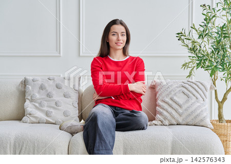 Portrait of beautiful young teenage girl sitting on sofa looking at camera Portrait of beautiful young teenage girl sitting on sofa looking at camera 142576343