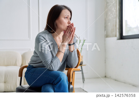 Depressed worried mature woman sitting on a chair, at home Depressed worried mature woman sitting on a chair, at home 142576358