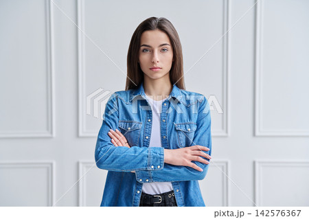 Happy confident young woman in denim shirt with arms crossed against white background 142576367