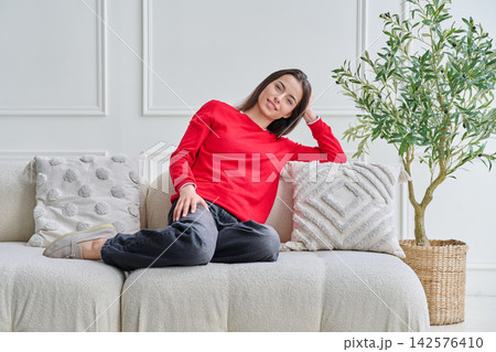 Portrait of beautiful young teenage girl sitting on sofa looking at camera 142576410