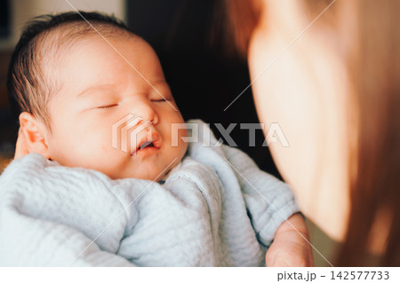 明るい部屋で愛情たっぷりの母親の手に抱かれる赤ちゃん 142577733