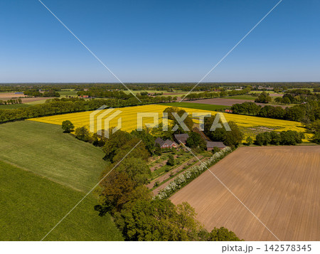 High angle wide horizontal aerial drone photograph of farmstead, yellow rapeseed field, orchard, and tilled soil in rural Gelderland, Achterhoek, Netherlands on sunny spring day High angle wide horizontal aerial drone photograph of farmstead, yellow rapeseed field, orchard, and tilled soil in rural Gelderland, Achterhoek, Netherlands on sunny spring day 142578345