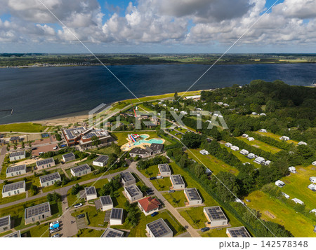 High angle wide horizontal aerial drone photograph of lakeside holiday resort, solar chalets, outdoor pool complex, campsite, and Lake Veere in Kamperland, Zeeland, Netherlands on sunny summer day 142578348