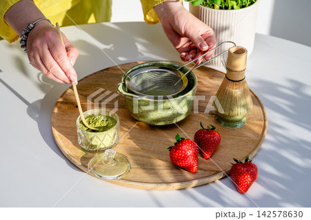 Authentic Moment of Stirring Matcha with Strawberries. Authentic candid moment of stirring matcha in ceramic bowl alongside strawberries on kitchen cutting board. Motion and warmth of whisking with ba Authentic Moment of Stirring Matcha with Strawberries. Authentic candid moment of stirring matcha in ceramic bowl alongside strawberries on kitchen cutting board. Motion and warmth of whisking with ba 142578630