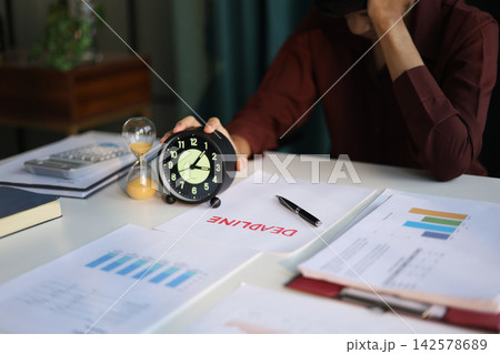 Businessman working on office desk, holding clock with deadline document and running hourglass on the table. Time management concept. 142578689