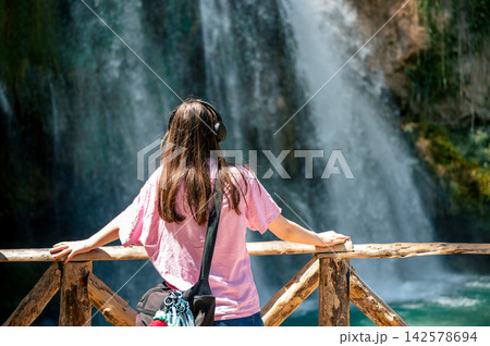 Teen Girl Admiring a Waterfall in Summer. A teenage girl admires a waterfall from a wooden viewpoint in the lush Monasterio de Piedra natural park in Aragon, Spain, a young traveler enjoying a peacefu Teen Girl Admiring a Waterfall in Summer. A teenage girl admires a waterfall from a wooden viewpoint in the lush Monasterio de Piedra natural park in Aragon, Spain, a young traveler enjoying a peacefu 142578694