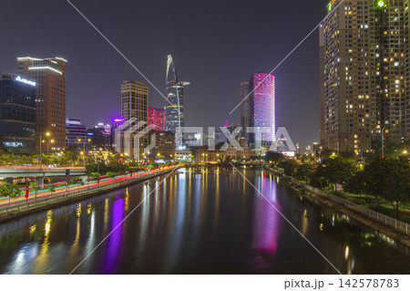 High-rise buildings, colorful city lights, traffic trails, and reflections fill an urban waterfront scene at night. 142578783