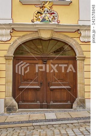 Large wooden double door with arched window and decorative coat of arms on building facade 142578848