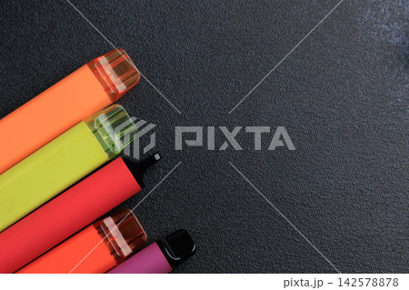 Different types of electronic cigarettes on a black surface with a clear layout showing colors and designs of the devices 142578878