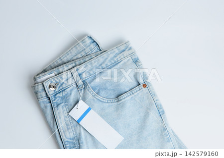 Pair of light blue jeans with a tag placed neatly on a white background during daytime hours 142579160