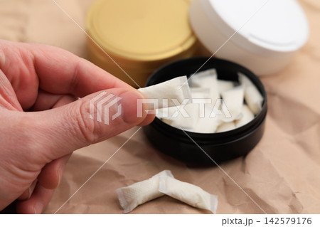 Snus pouches are held in one hand with containers in background showing different flavors and types near a brown surface 142579176