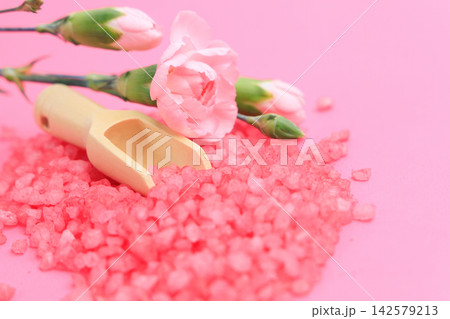 Bright pink salt and fresh flowers on a pink background with a wooden scoop in the middle on a sunny day Bright pink salt and fresh flowers on a pink background with a wooden scoop in the middle on a sunny day 142579213