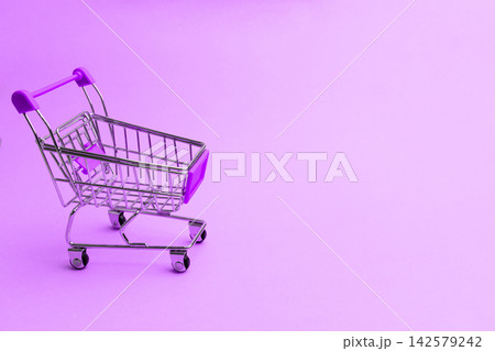Shopping cart on a purple background with a simple design and bright colors in a retail setting for modern merchandise display Shopping cart on a purple background with a simple design and bright colors in a retail setting for modern merchandise display 142579242