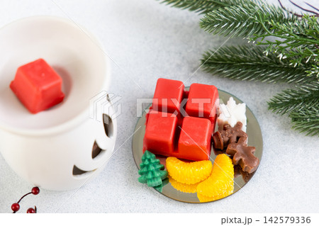 Warm glow from aroma lamp with Christmas wax melts on a table with decorative items Warm glow from aroma lamp with Christmas wax melts on a table with decorative items 142579336