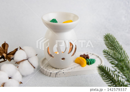 Aroma lamp with Christmas wax melts sits on a table with cotton and pine branches nearby Aroma lamp with Christmas wax melts sits on a table with cotton and pine branches nearby 142579337