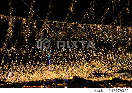 String lights hang from above at a Christmas festive event at night creating a bright atmosphere for people below String lights hang from above at a Christmas festive event at night creating a bright atmosphere for people below 142579353