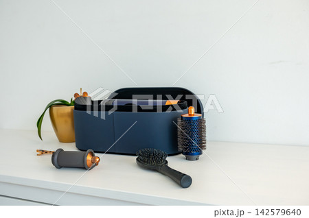 Hair styler case and accessories side profile on dresser. Side profile view of navy hair styler case with accessories arranged alongside on white dresser, beauty tools lineup for hair care product Hair styler case and accessories side profile on dresser. Side profile view of navy hair styler case with accessories arranged alongside on white dresser, beauty tools lineup for hair care product 142579640