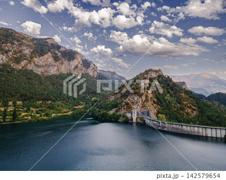 Lanuza Dam Beneath Dramatic Pyrenees Clouds. Aerial view of the Lanuza dam and reservoir beneath dramatic clouds in the Spanish Pyrenees near Formigal, Spain, the concrete barrier holding turquoise wa Lanuza Dam Beneath Dramatic Pyrenees Clouds. Aerial view of the Lanuza dam and reservoir beneath dramatic clouds in the Spanish Pyrenees near Formigal, Spain, the concrete barrier holding turquoise wa 142579654