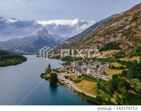 Pyrenees Village and Twin Peaks of Foratata. Aerial view of a Pyrenees village beside the turquoise Lanuza reservoir with the twin summits of Pena Foratata behind near Formigal, Spain, a scenic mounta Pyrenees Village and Twin Peaks of Foratata. Aerial view of a Pyrenees village beside the turquoise Lanuza reservoir with the twin summits of Pena Foratata behind near Formigal, Spain, a scenic mounta 142579712