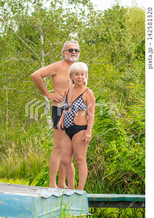 Senior couple standing in swimsuits beside lush outdoor greenery Senior couple standing in swimsuits beside lush outdoor greenery 142581320