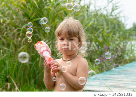 Thoughtful toddler holding bubble wand in lush summer garden Thoughtful toddler holding bubble wand in lush summer garden 142581332
