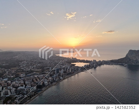 serene sunset over coastal city with buildings, beach, water, mountains and concrete, sand, rock, orange, blue, urban landscape, aerial view, travel, real estate, vacation rentals. serene sunset over coastal city with buildings, beach, water, mountains and concrete, sand, rock, orange, blue, urban landscape, aerial view, travel, real estate, vacation rentals. 142582352