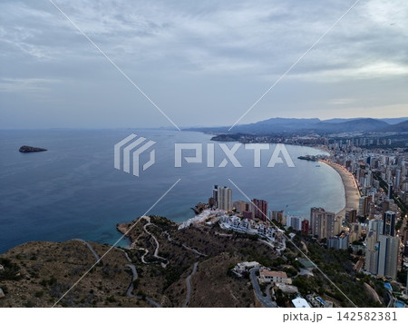 Coastal skyline with crescent beach, calm sea, waterfront towers, and distant rocky island under soft dusk light, with coast, city, skyline, beach detail, showing dusk, sea, island, waterfront context Coastal skyline with crescent beach, calm sea, waterfront towers, and distant rocky island under soft dusk light, with coast, city, skyline, beach detail, showing dusk, sea, island, waterfront context 142582381