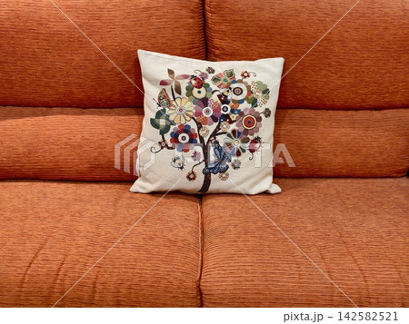 embroidered pillow resting on a cozy couch in a living room top-down view with orange and white fabric and thread, creating a warm and decorative interior design. embroidered pillow resting on a cozy couch in a living room top-down view with orange and white fabric and thread, creating a warm and decorative interior design. 142582521