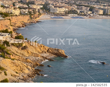 relaxed scenic view of rocky coastline with cliffs and beachside town in aerial perspective, featuring palm trees and concrete buildings under blue and tan skies. 142582535