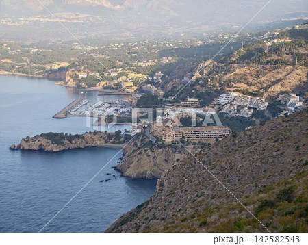 peaceful coastal town stationary aerial view with buildings, harbor, rocky cliffs, and trees in marina landscape under blue and green sky during daytime period. peaceful coastal town stationary aerial view with buildings, harbor, rocky cliffs, and trees in marina landscape under blue and green sky during daytime period. 142582543