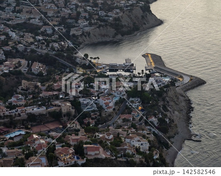peaceful coastal town with stationary aerial view of houses, pools, roads, and trees on cliffside area by water period. real estate, vacation rentals, serene, modern, bright. peaceful coastal town with stationary aerial view of houses, pools, roads, and trees on cliffside area by water period. real estate, vacation rentals, serene, modern, bright. 142582546