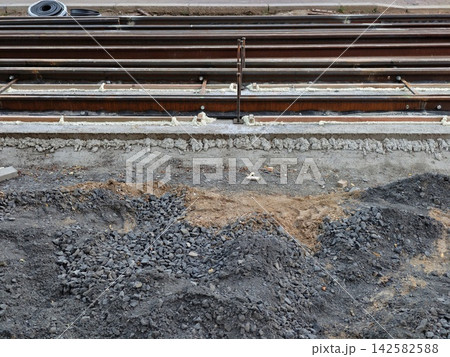 construction of urban railroad tracks on a ground-level perspective with concrete sleepers and gravel ballast in an industrial setting, featuring gray and brown tones. construction of urban railroad tracks on a ground-level perspective with concrete sleepers and gravel ballast in an industrial setting, featuring gray and brown tones. 142582588