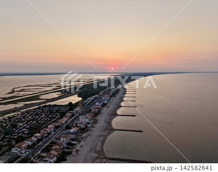 serene sunset over coastal town with beach and wetlands, aerial view of houses and roads, orange and pink sky, sand and water, concrete structures, travel and vacation rental context. serene sunset over coastal town with beach and wetlands, aerial view of houses and roads, orange and pink sky, sand and water, concrete structures, travel and vacation rental context. 142582641