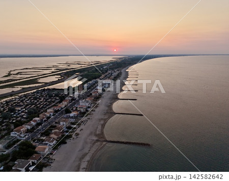 peaceful sunset over coastal town at dusk with aerial view of buildings and roads by the beachside town at dusk with concrete, sand, and metal materials and orange and pink colors. peaceful sunset over coastal town at dusk with aerial view of buildings and roads by the beachside town at dusk with concrete, sand, and metal materials and orange and pink colors. 142582642